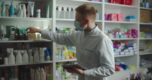 Egy gyógyszerész orvosi maszkban tanácsot ad egy vevőnek egy gyógyszertárban. Gyógyszerek vásárlása a vírus alatt. — Stock videók