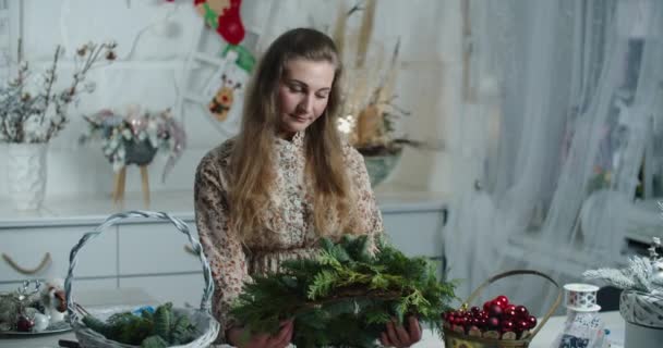 Haciendo una corona rústica de Navidad. Mujer sosteniendo ramas verdes sobre fondo rústico de madera. Taller de vacaciones de temporada en línea, haciendo decoraciones festivas en casa — Vídeo de stock