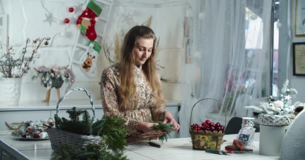 Kırsal Noel çelengi yapıyorum. Kırsal ahşap arka planda yeşil dallar tutan bir kadın. Mevsimlik tatil atölyesi çevrimiçi, evde şenlikli dekorasyonlar yapılıyor. — Stok video