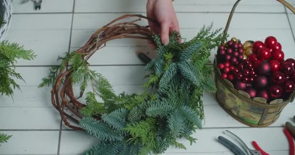 Rustykalny świąteczny wieniec. Ręce trzymające zielone gałęzie na rustykalnym drewnianym tle. Sezonowe warsztaty wakacyjne online, co świąteczne dekoracje w domu — Wideo stockowe