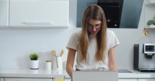Uma jovem fica perto da mesa em casa e trabalha em um laptop. Imprimir texto. Trabalho em casa — Vídeo de Stock
