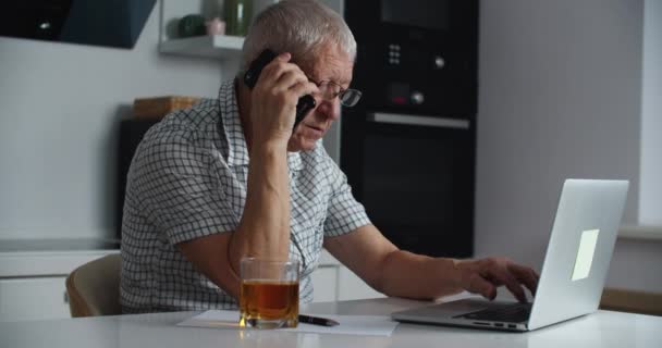 Detailní záběr muže středního věku s brýlemi pracuje na notebooku a mluví na mobilu. Práce z domova. Mužský portrét — Stock video