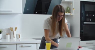 Gözlüklü genç bir kadın evdeki masada dizüstü bilgisayarla çalışıyor. Bazen meyve suyu içer. Evden çalış.