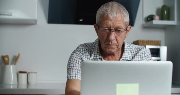 Κουρασμένος ηλικιωμένος άνδρας με γυαλιά εργάζεται σε ένα φορητό υπολογιστή στο σπίτι, βγάζει τα γυαλιά του και κάνει μασάζ προσώπου από την κούραση. Πορτραίτο ενός άνδρα. — Αρχείο Βίντεο