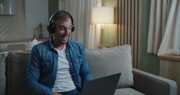 Headphone Man duduk di sofa di depan pc berbicara dengan mitra bisnis dengan panggilan video jauh memecahkan masalah bekerja sama jarak jauh karena karantina coronavirus, on-line tutoring konsep — Stok Video