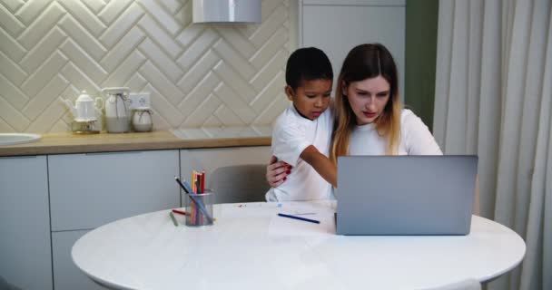 Çok ırklı Avrupalı anne ve Afrikalı Amerikalı oğul evde birlikte vakit geçiriyorlar. Annesi evde çalışırken küçük oğlu resim çiziyor. — Stok video