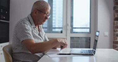 Dizüstü bilgisayar kullanan gözlüklü son sınıf öğrencisi online alışveriş yapıyor ve kredi kartıyla ödeme yapıyor. Ev mutfağı.