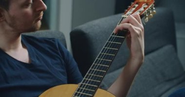 Genç bir adam kanepede oturur ve gitar çalar. Elinde gitar olan bir adamın yakın plan portresi..