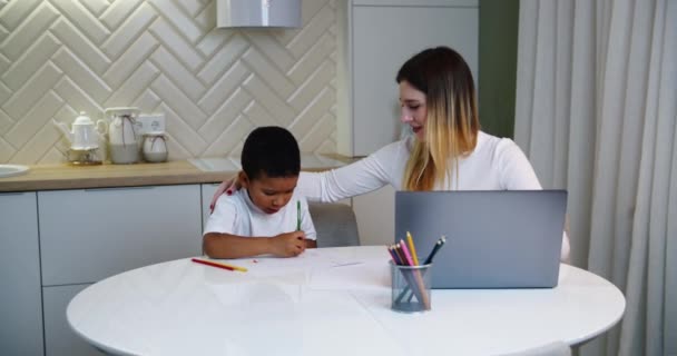 Família multiétnica mãe europeia e filho afro-americano passam tempo juntos em casa. Pequeno filho desenha quando a mãe trabalha em casa — Vídeo de Stock