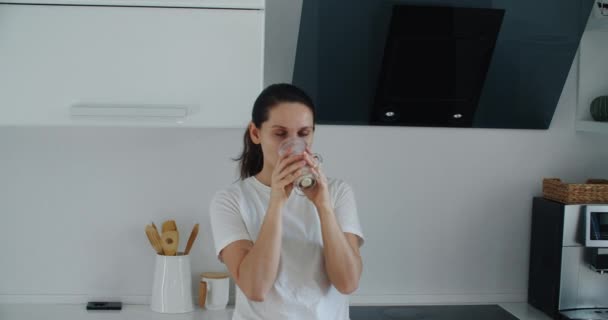 Een vrouw in huiskleding drinkt smoothies gemaakt van fruit en groenten in de keuken vroeg in de ochtend. Zorgen voor uw gezondheid en lichaam. — Stockvideo