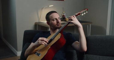 Genç bir adam kanepede oturur ve gitar çalar. Elinde gitar olan bir adamın yakın plan portresi..