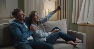 Kanepede oturan sevimli, neşeli, pozitif stil sahibi eşlerin yakın plan portresi. Karı koca modern aydınlık dairelerde telefonda selfie çekiyorlar.