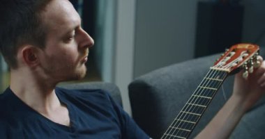 Genç bir adam kanepede oturur ve gitar çalar. Elinde gitar olan bir adamın yakın plan portresi..