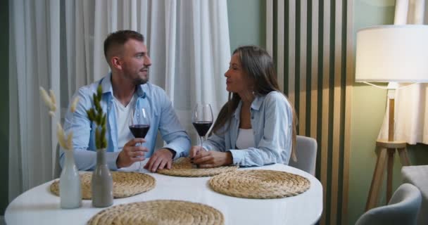 Lachend paar praten lachen vieren verjaardag op date met een bril drinken rode wijn, gelukkig man en vrouw zitten in de keuken — Stockvideo