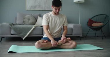 Nilüfer pozunda yoga minderinde oturan, gözlerini kapayan ve namaste 'de el ele tutuşan koyu renk saçlı yakışıklı genç adam. Meditasyon ve konsantrasyon