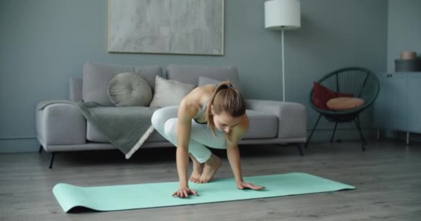 Sportlich glückliche schöne junge Frau praktiziert Yoga, macht Armstand, asymmetrischer Armausgleich, trainiert in weißer Sportbekleidung, zu Hause, in voller Länge — Stockvideo