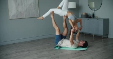Genç bir beyaz erkek ve kadın çift evde akrobatik yoga yapıyor. Etkinlik zorluğu.