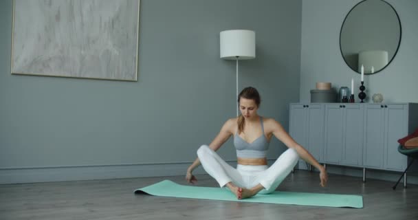 Yoga em casa. Jovem mulher atraente senta-se no tapete em casa durante a aula. — Vídeo de Stock