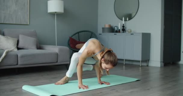 Sportlich glückliche schöne junge Frau praktiziert Yoga, macht Armstand, asymmetrischer Armausgleich, trainiert in weißer Sportbekleidung, zu Hause, in voller Länge — Stockvideo