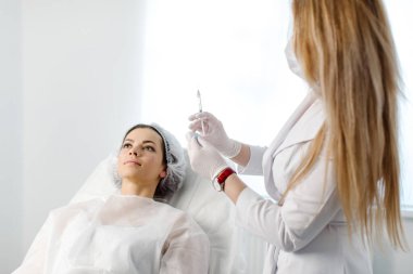 Çekici genç bir kadın canlandırıcı yüz enjeksiyonu yaptırıyor. O, klinikte sakince oturuyor. Uzman güzellik uzmanı hyaluronik asitle kadın kırışıklıklarını dolduruyor..