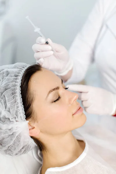 Çekici genç bir kadın canlandırıcı yüz enjeksiyonu yaptırıyor. O, klinikte sakince oturuyor. Uzman güzellik uzmanı hyaluronik asitle kadın kırışıklıklarını dolduruyor..