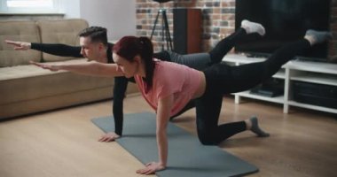 Kaslı atletik adam ve spor elbiseli güzel kadın dairelerinde minimalist iç mekan ile egzersiz yapıyorlar..