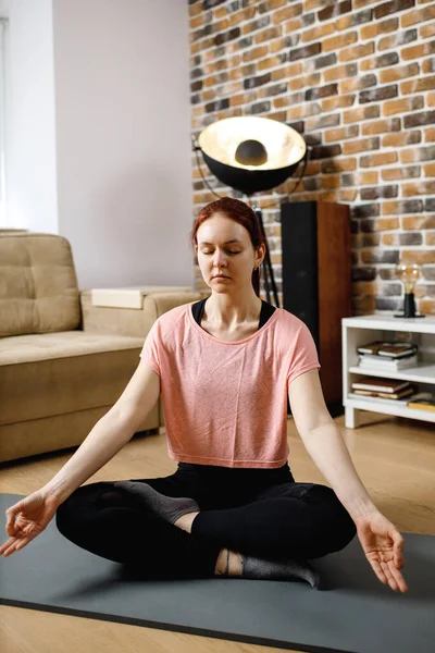 Calm woman meditating, listening spiritual practices lessons , sitting on lotus pose at home. Yoga concept.