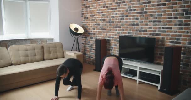 Muscular athletic man and beautiful fitness woman in workout clothes are doing exercises in their apartment with minimalistic Interior. — Stock Video