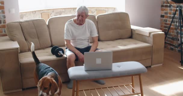 Homme adulte et mature senior travaillant son corps avec haltère un homme heureux formation à l'intérieur assis sur le canapé — Video