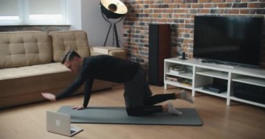 Evde antrenman. Sportif adam yoga yaparken çevrimiçi özel ders izliyor, oturma odasında egzersiz yapıyor, boş yer var.