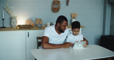 Mutlu Afrikalı baba ve küçük oğlu evde dizüstü bilgisayar kullanıyor, internetten film izliyor ya da internette geziniyor.
