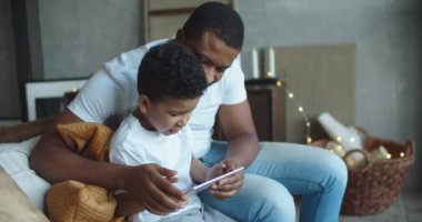 Mutlu Afrikalı baba ve küçük oğlu evde dizüstü bilgisayar kullanıyor, internetten film izliyor ya da internette geziniyor.