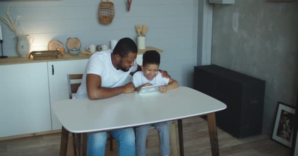 Feliz padre africano y su hijo pequeño usando el ordenador portátil en casa juntos, viendo películas en línea o navegando por Internet — Vídeos de Stock