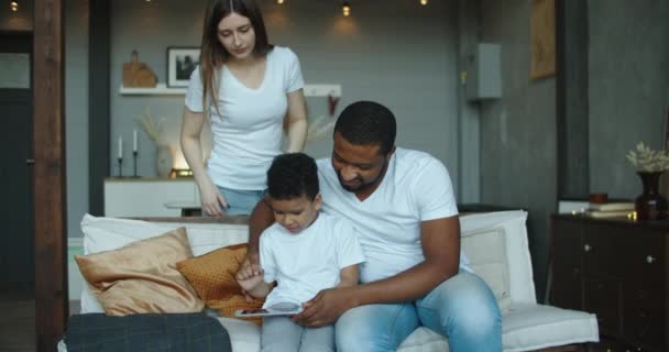 Pai africano feliz e seu filho usando laptop em casa juntos, assistindo filmes on-line ou navegando na internet com a mãe — Vídeo de Stock