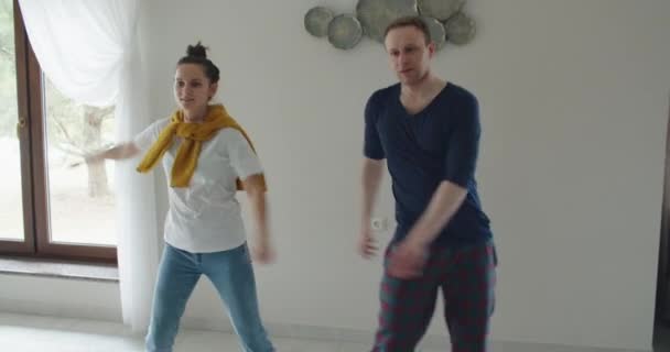 Um homem e uma mulher dançam em frente a uma TV, parodiam e repetem o que mostram na TV — Vídeo de Stock