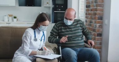 Evde konuşurken tekerlekli sandalyedeki hastaya bilgi veren genç bir hemşire. Salgın ve virüs kavramı