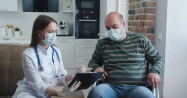 Evde konuşurken tekerlekli sandalyedeki hastaya bilgi veren genç bir hemşire. Salgın ve virüs kavramı