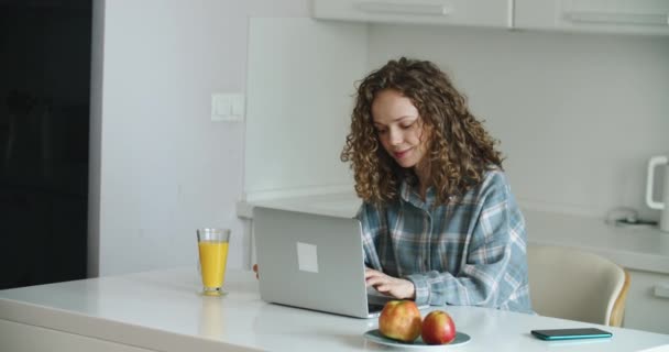 Mulher feliz usando laptop no balcão em casa na cozinha. A trabalhar em casa em quarentena. Distanciamento social Auto-isolamento — Vídeo de Stock
