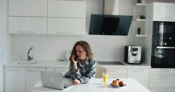 Mulher feliz usando laptop no balcão em casa na cozinha. A trabalhar em casa em quarentena. Distanciamento social Auto-isolamento — Vídeo de Stock