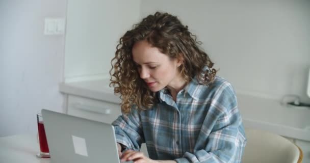 Een vrolijke vrouw die thuis in de keuken een laptop gebruikt. Ik werk vanuit huis in quarantaine. Sociale afstandelijkheid Zelfisolatie — Stockvideo