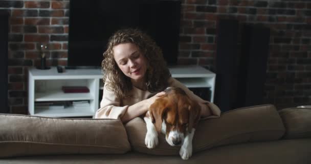 ผู้หญิงนั่งกับสุนัขบนโซฟา ยิ้มและจังหวะ . — วีดีโอสต็อก