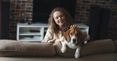 Kız kanepede köpekle oturuyor, gülümsüyor ve okşuyor.. 