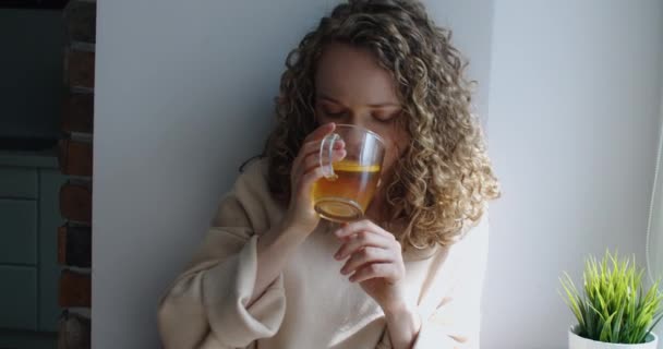 Happy woman with curly hair is drinking tea and typing a message on a laptop. Sunny day. — Stock Video