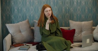Kızıl saçlı genç kız bir cep telefonundan sesli mesaj kaydediyor. Evde çalışıyorum..