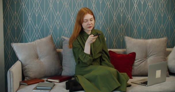 Una giovane studentessa con i capelli rossi registra un messaggio vocale su un telefono cellulare. Lavorare a casa. — Video Stock