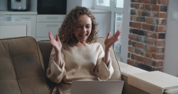 Mulher feliz com cabelo encaracolado lê boas notícias no laptop. Vitória, vitória. Chame um amigo para compartilhar as notícias — Vídeo de Stock