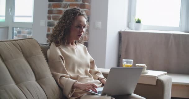 Glückliche Frau mit lockigem Haar liest gute Nachrichten auf Laptop. Sieg, Sieg. — Stockvideo
