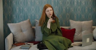 Kızıl saçlı genç kız bir cep telefonundan sesli mesaj kaydediyor. Evde çalışıyorum..