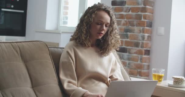 Happy woman with curly hair finished work on laptop. And drinks tea while looking out the window — Stock Video
