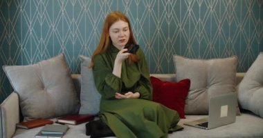 Kızıl saçlı genç kız bir cep telefonundan sesli mesaj kaydediyor. Evde çalışıyorum..